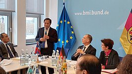 Laotischer Repräsentant hält Vortrag an einem Besprechungstisch vor EU- und Deutschlandfahne